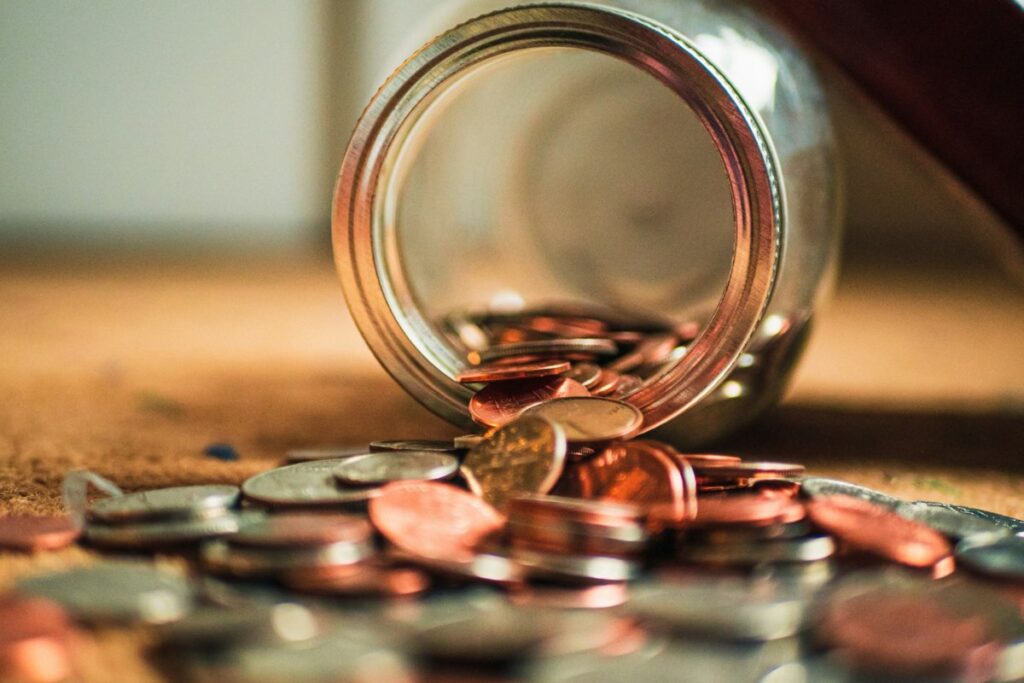 Moedas espalhadas saindo de um pote de vidro, simbolizando valor e reconhecimento.