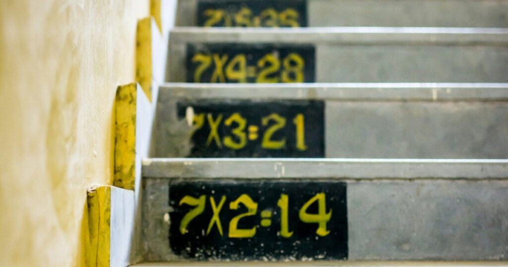 Degraus de uma escada com tabuadas de multiplicação pintadas, simbolizando aprendizado e progressão.