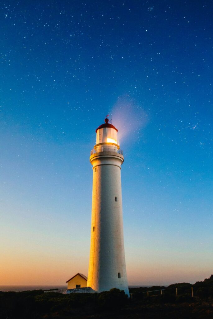Farol iluminado sob um céu estrelado ao entardecer, simbolizando liderança e potencialização de pessoas nas organizações.